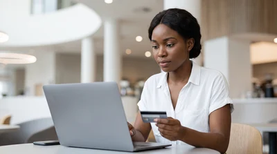 A woman sits focused with a laptop and a small, generic electronic toll tag in a modern lounge environment.
