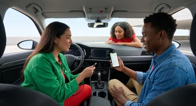 Friends in a modern grey Volkswagen Jetta in an Orlando lot check the dashboard screen for wireless phone connectivity.
