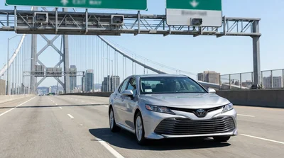 Driver in a white car rental approaching a toll plaza on a New York bridge