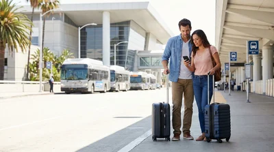 Travelers with luggage waiting for a car rental shuttle outside LAX Terminal 6 in Los Angeles