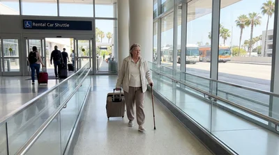 Passenger with a suitcase using a ramp to board a car rental shuttle bus at a Los Angeles terminal