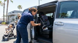 Parent checking a child seat in the backseat of a car rental parked on a California street