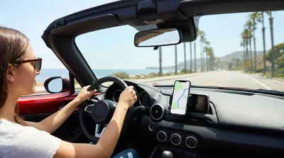 Hands-free smartphone mounted on the dashboard of a car rental driving along a sunny California highway