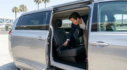 Parent securing a child safety seat in the back of a car rental parked on a sunny California street
