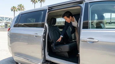 Parent securing a child safety seat in the back of a car rental parked on a sunny California street
