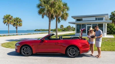 White car hire driving along a sunny coastal highway lined with palm trees in Florida