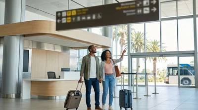 Travelers with luggage waiting for a car rental shuttle outside LAX Terminal 1 in Los Angeles