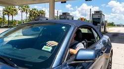 Driver in a car rental approaching a SunPass toll plaza on a sunny Florida highway