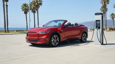 White electric car rental connected to a public EV charging station in a sunny California parking lot