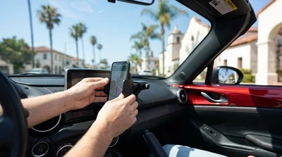Smartphone securely mounted on the windshield of a car rental with a sunny California highway visible ahead
