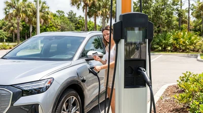 White electric car rental plugged into a public charging station near palm trees in Florida