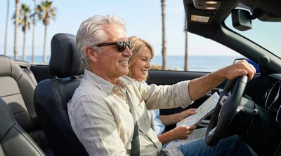 Smiling senior couple driving a car rental along a scenic coastal highway in California