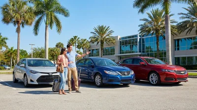 Several different sized cars parked in a row under palm trees at a sunny Orlando car rental lot