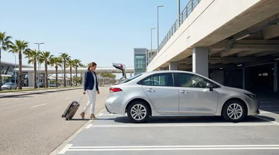 Traveler with luggage approaching a car rental desk at a Los Angeles airport terminal
