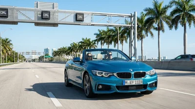 White car rental driving under an electronic toll gantry on a sunny highway in Miami