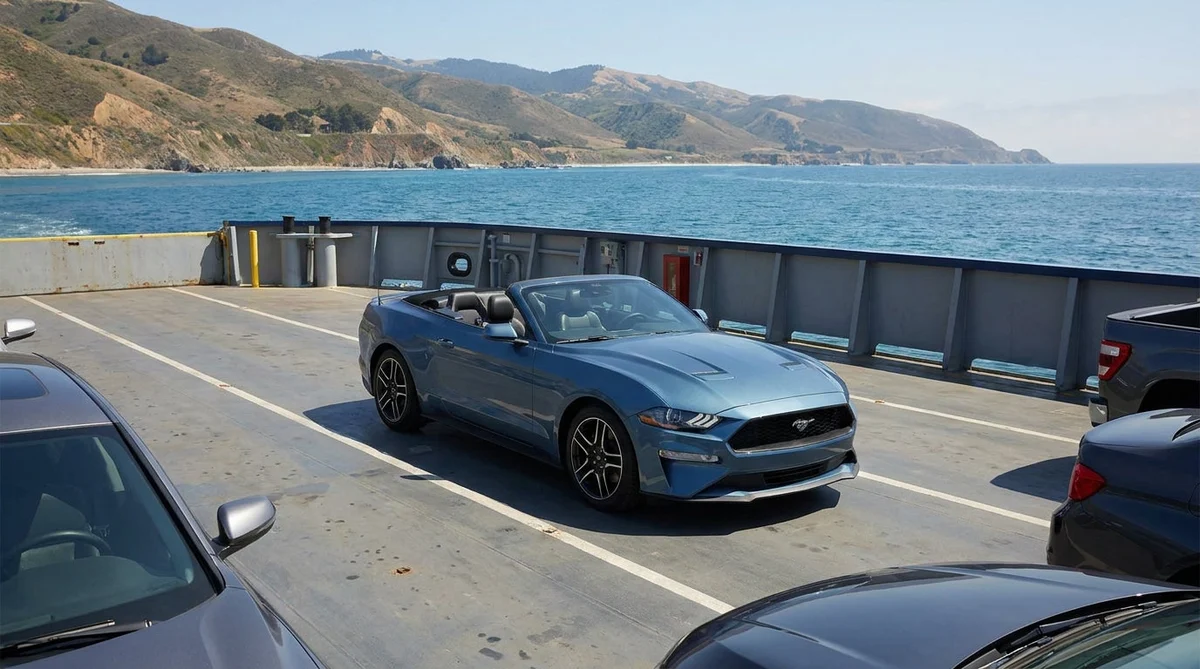 A car rental parked on the open deck of a ferry crossing the water along the California coast