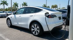 White electric car plugged into a charging station at a sunny car rental lot in Florida