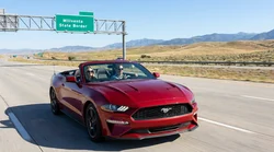 A white car rental traveling past a Welcome to California sign on a sunny desert highway