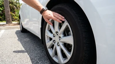 Close-up of a damaged wheel and hubcap on a silver car hire parked under palm trees in Florida
