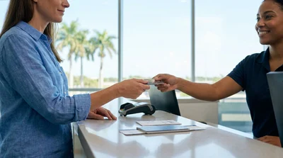 Customer handing a credit card to a staff member at a bright car hire desk in Florida