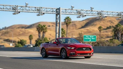 Person driving a silver car rental on a sunny California highway approaching an overhead toll gantry