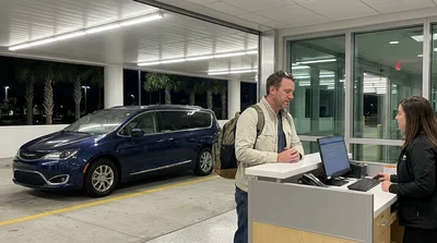 Traveler with luggage standing at a brightly lit car rental counter in Orlando airport at night