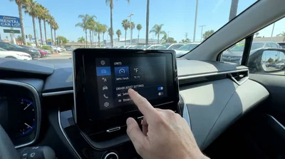 Driver adjusting digital dashboard settings inside a car rental with a scenic California highway out the windshield