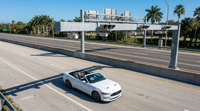 A white car rental passing under an electronic toll gantry on a sunny Florida highway