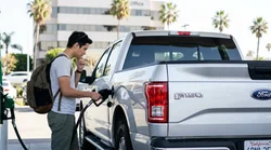 Driver pumping gas into a white car rental at a sunlit Los Angeles fuel station