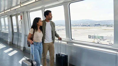 Passengers with rolling luggage walking under directional signs toward the car rental center in San Francisco