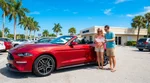 Two people driving a car rental along a sunny palm-lined highway in Florida