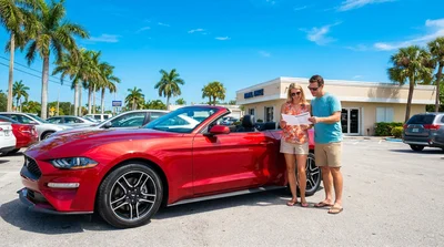 Two people driving a car rental along a sunny palm-lined highway in Florida