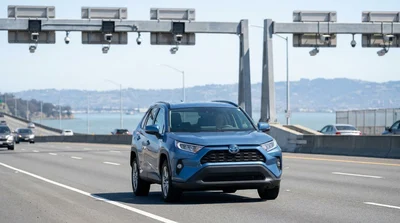 White car rental approaching a bridge toll plaza in San Francisco under a blue sky