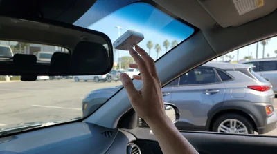 Person checking a FasTrak toll tag on the windshield of a car rental at a pickup lot in California
