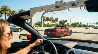 Driver in a white car rental passing through a sunlit highway toll plaza in Florida