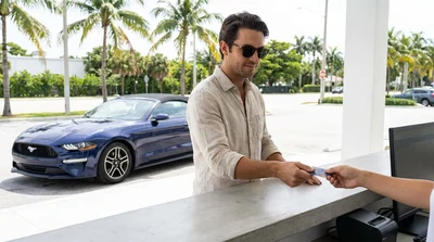 Close up of a hand holding a debit card in front of a car hire vehicle in Miami