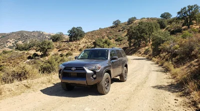 White car rental driving on an unpaved dirt road through a dry California desert landscape