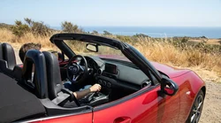 Hand shifting a manual transmission stick shift inside a car rental on a sunny California coastal highway