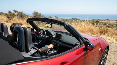 Hand shifting a manual transmission stick shift inside a car rental on a sunny California coastal highway