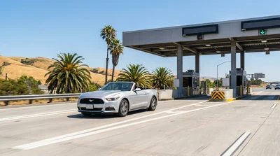 White car rental driving on a California highway approaching a toll plaza sign