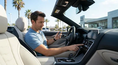 Hand pressing a dashboard start button inside a car rental with sunny California palm trees visible outside