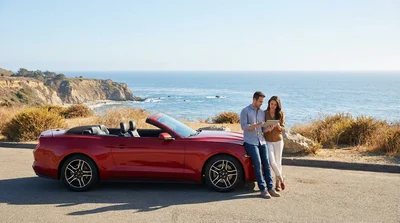 Person driving a car rental along a sunny coastal highway in California