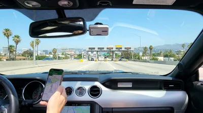 Rear view of a car rental driving under an electronic toll camera on a sunny highway in Los Angeles