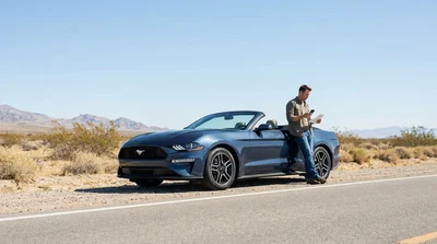 Driver inspecting the engine of a broken down car rental on a desert highway near Las Vegas