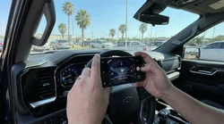 Person holding a smartphone to photograph a car rental dashboard showing the fuel gauge and odometer in Texas
