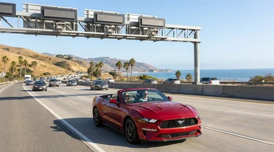 Silver car rental driving past an electronic toll plaza on a sunny California highway