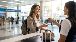 Traveler with luggage receiving keys at a car rental counter in Los Angeles