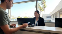 Close-up of a customer handing a credit card to an agent at a car hire counter in Los Angeles