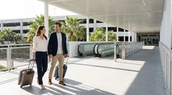 Traveler with a rolling suitcase walking toward a car rental counter inside a Florida airport
