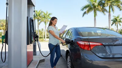 Person pumping gas into a white car rental at a sunny Florida gas station